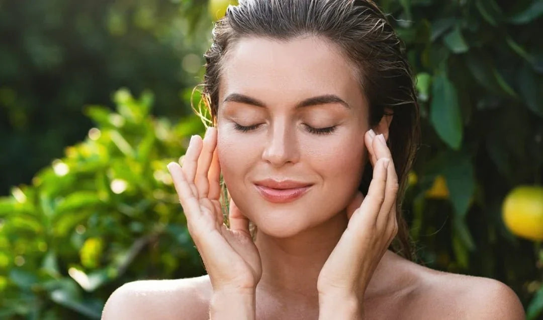 Woman with clear, glowing skin gently touching her face outdoors, skincare wellness concept