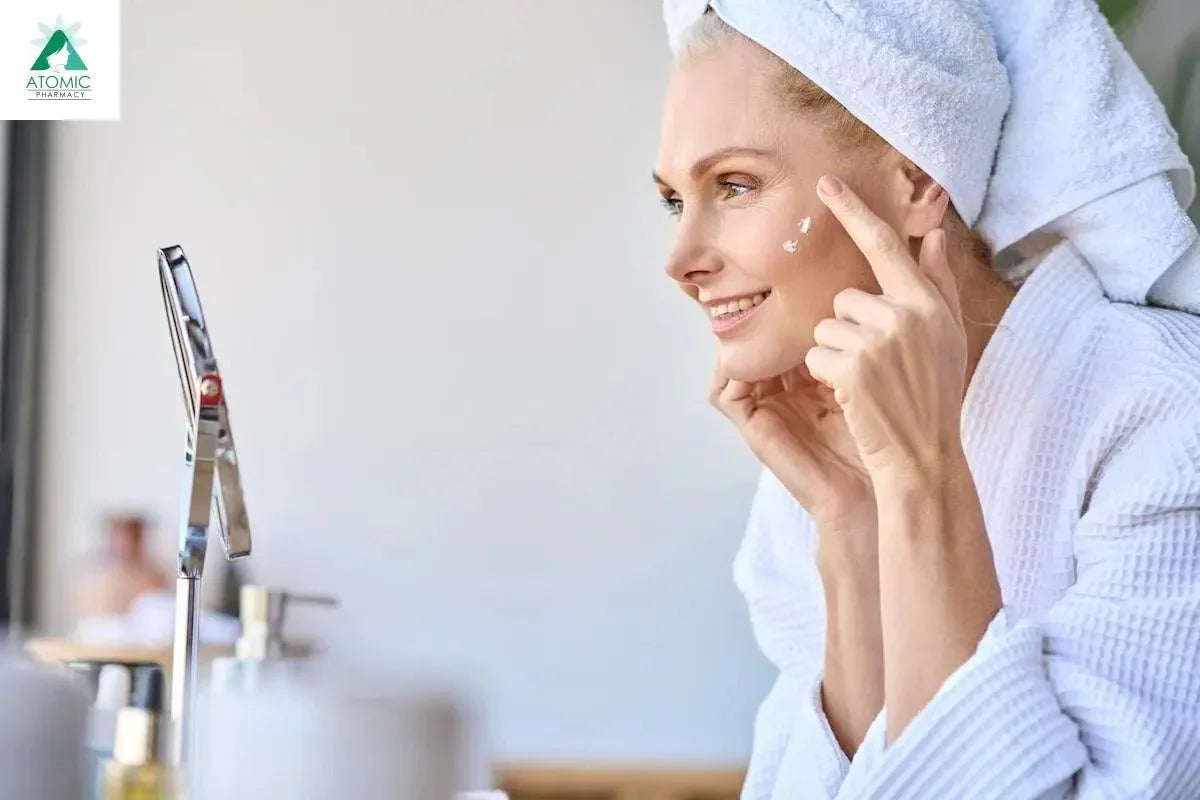 Woman in bathrobe applying anti-aging skincare cream to face in front of mirror