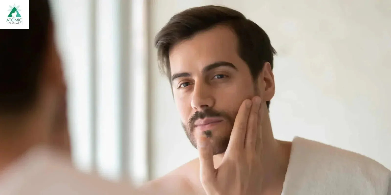Man applying skincare product to face in mirror, dermatologist-approved men's grooming routine