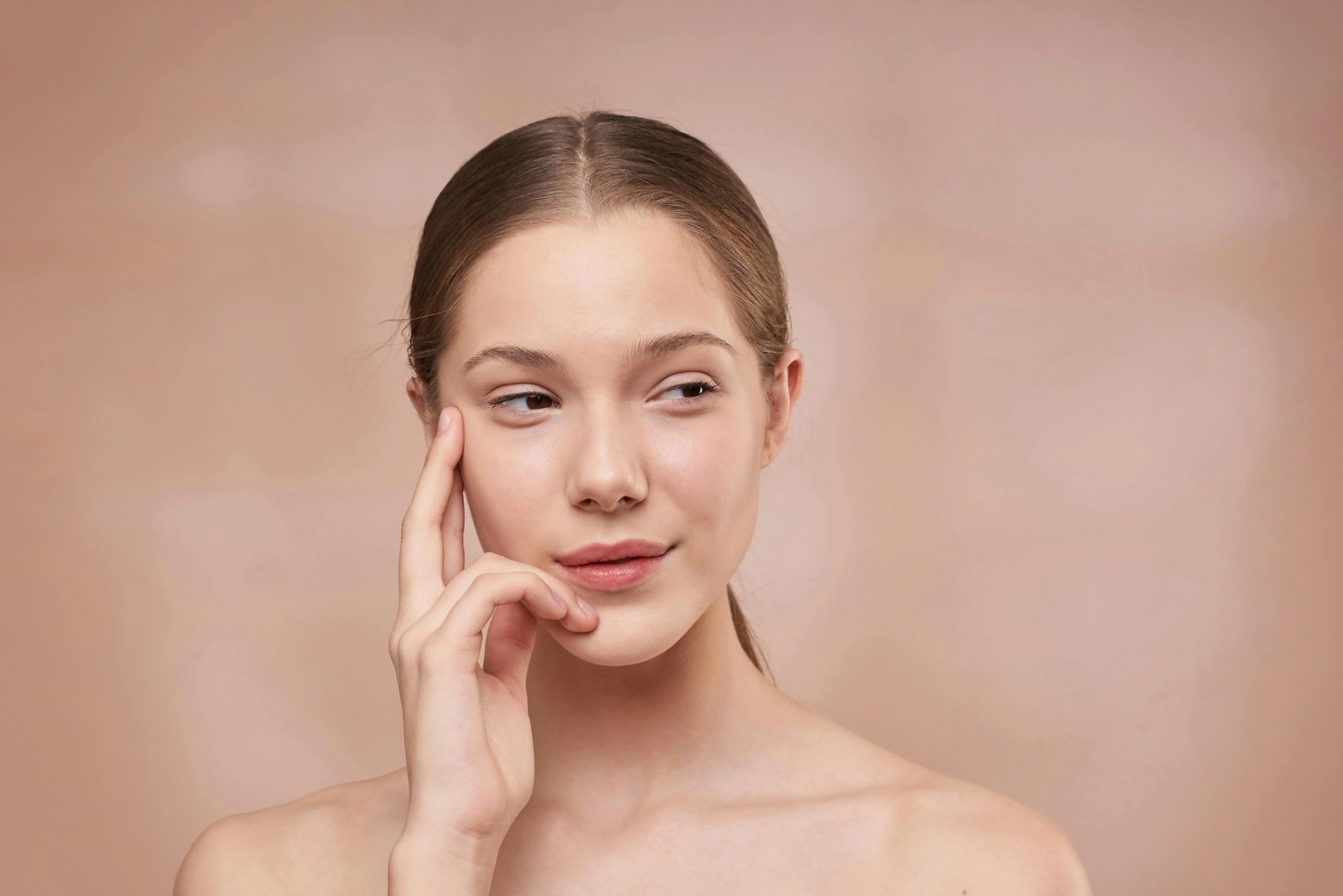 Young woman with clear skin touching face against neutral background, skincare concept